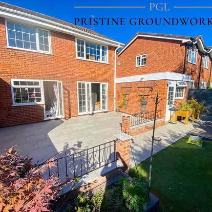 Porcelain patio and lawn behind a red brick house with black railings
